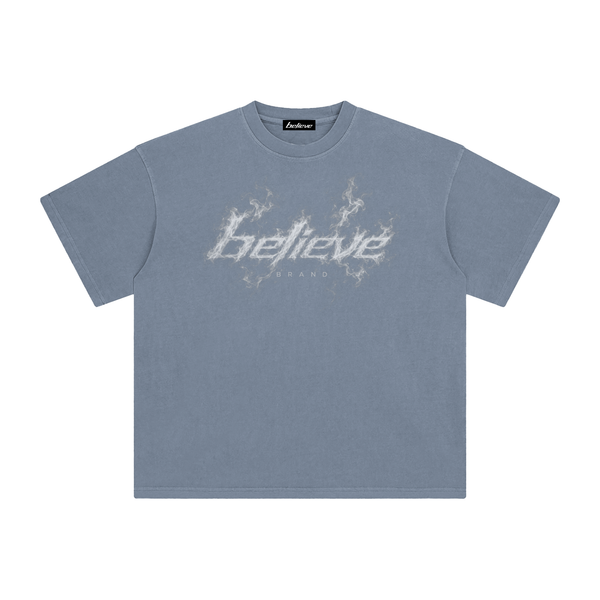 A slate blue crewneck t-shirt featuring a distressed white graphic on the chest that reads 'Believe' in a stylized font with lightning effects, displayed flat against a solid white background.